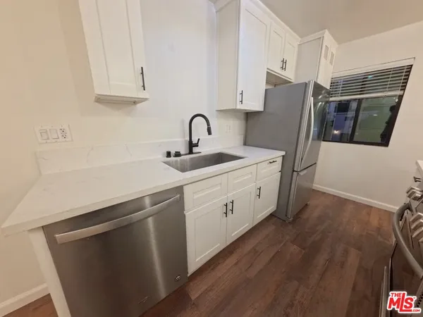 a kitchen with stainless steel appliances white cabinets a sink a stove a refrigerator and wooden floor