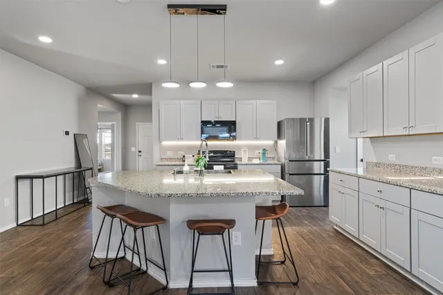 a kitchen with stainless steel appliances granite countertop a dining table chairs refrigerator and microwave