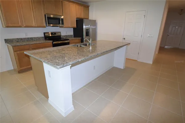 a kitchen with kitchen island granite countertop a sink a stove top oven a counter space and cabinets