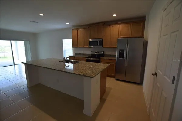 a kitchen with granite countertop a refrigerator a sink a stove a microwave a counter top space and cabinets