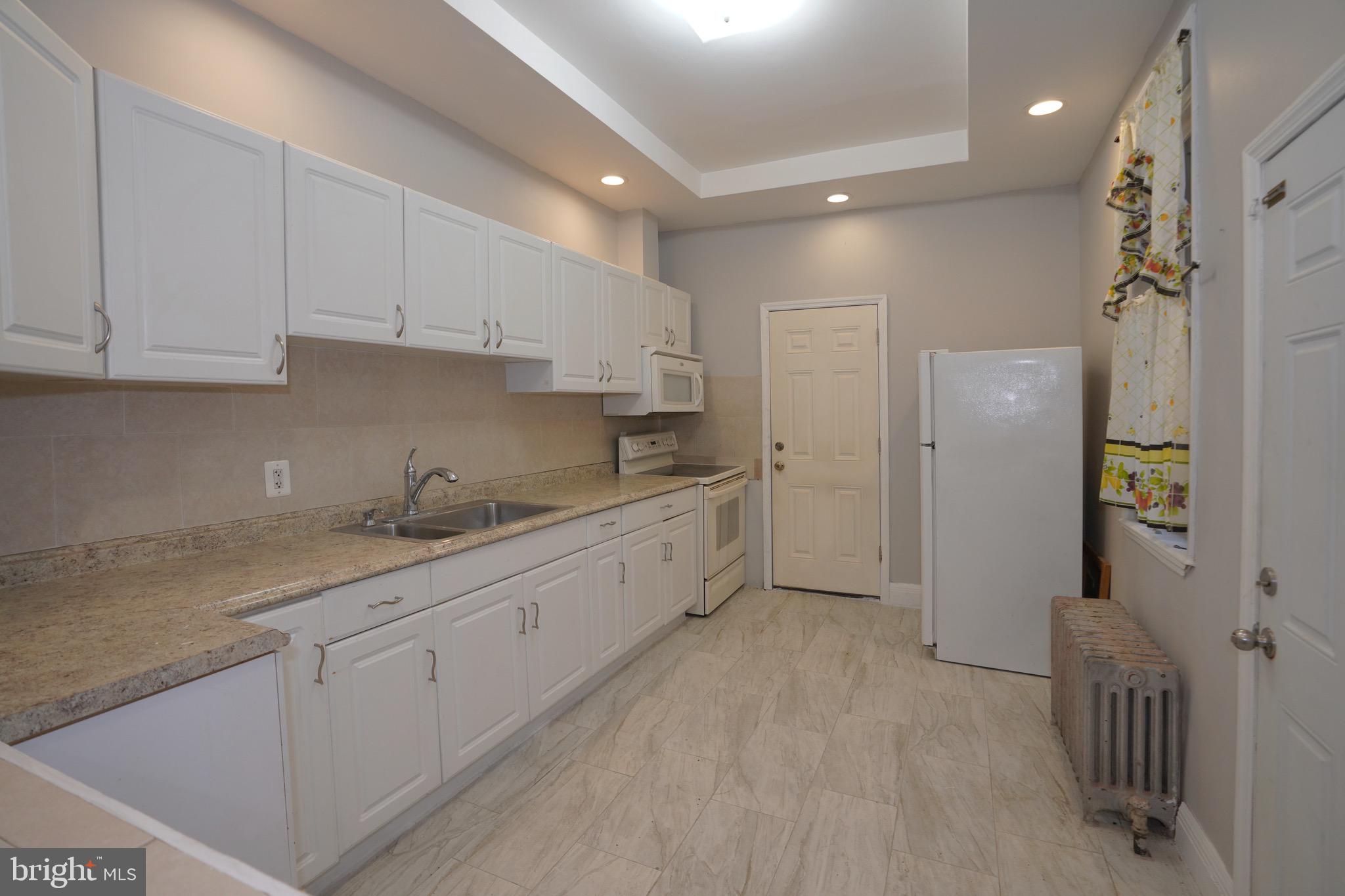 2512 North Front Street Philadelphia, PA 19133 - Photo 10 of 33 a large white kitchen with a sink a refrigerator and white cabinets