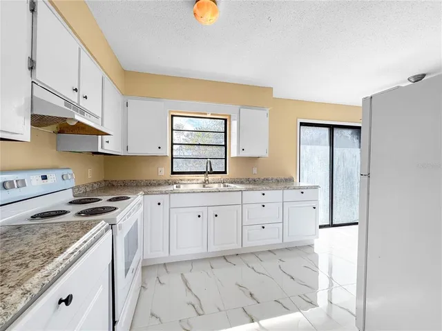 a large kitchen with granite countertop a refrigerator a sink a stove and white cabinets