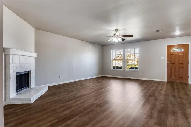 an empty room with wooden floor fireplace and windows