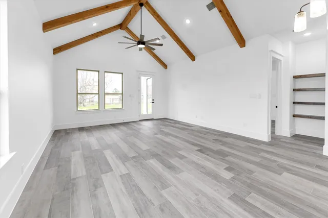 an empty room with wooden floor fan and windows