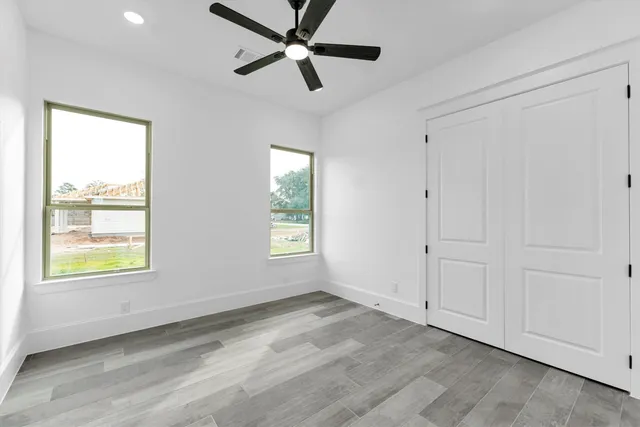 an empty room with wooden floor fan and windows