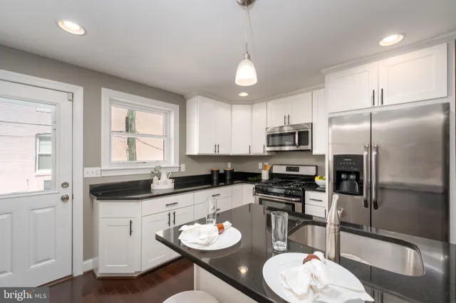 a kitchen with stainless steel appliances granite countertop a stove a refrigerator a sink a dining table and chairs with wooden floor