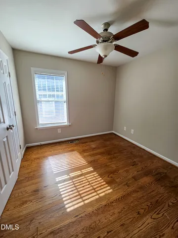 an empty room with wooden floor fan and windows