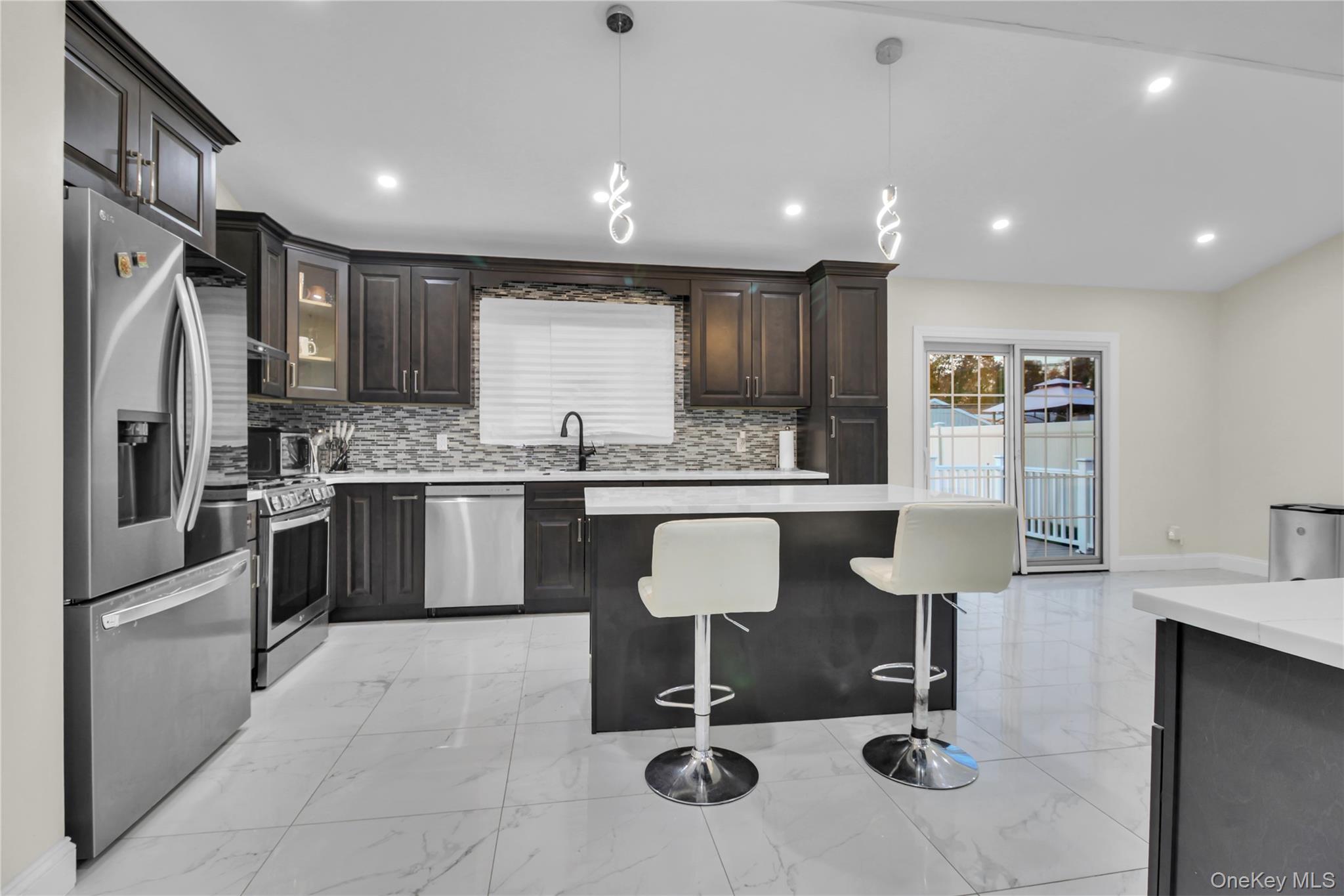 858 Prescott Street Valley Stream, NY 11580 - Photo 12 of 48 Kitchen with stainless steel appliances, light marble finish flooring, a breakfast bar, a kitchen island, and recessed lighting