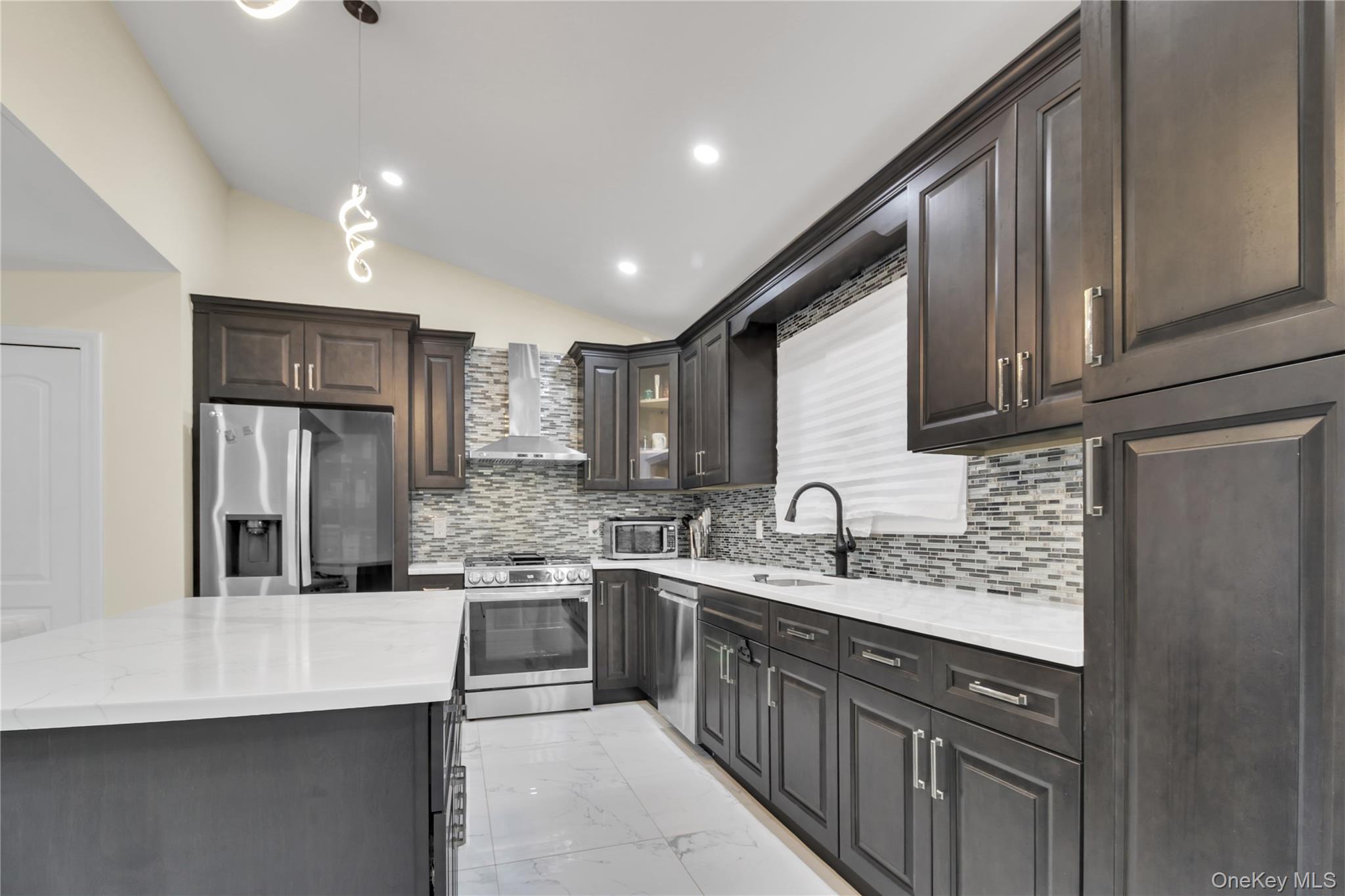 858 Prescott Street Valley Stream, NY 11580 - Photo 10 of 48 Kitchen featuring light marble finish floors, stainless steel appliances, pendant lighting, vaulted ceiling, and wall chimney exhaust hood