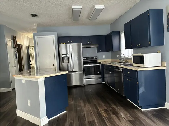 a kitchen with stainless steel appliances granite countertop a stove a sink dishwasher a refrigerator and a microwave oven with wooden floor