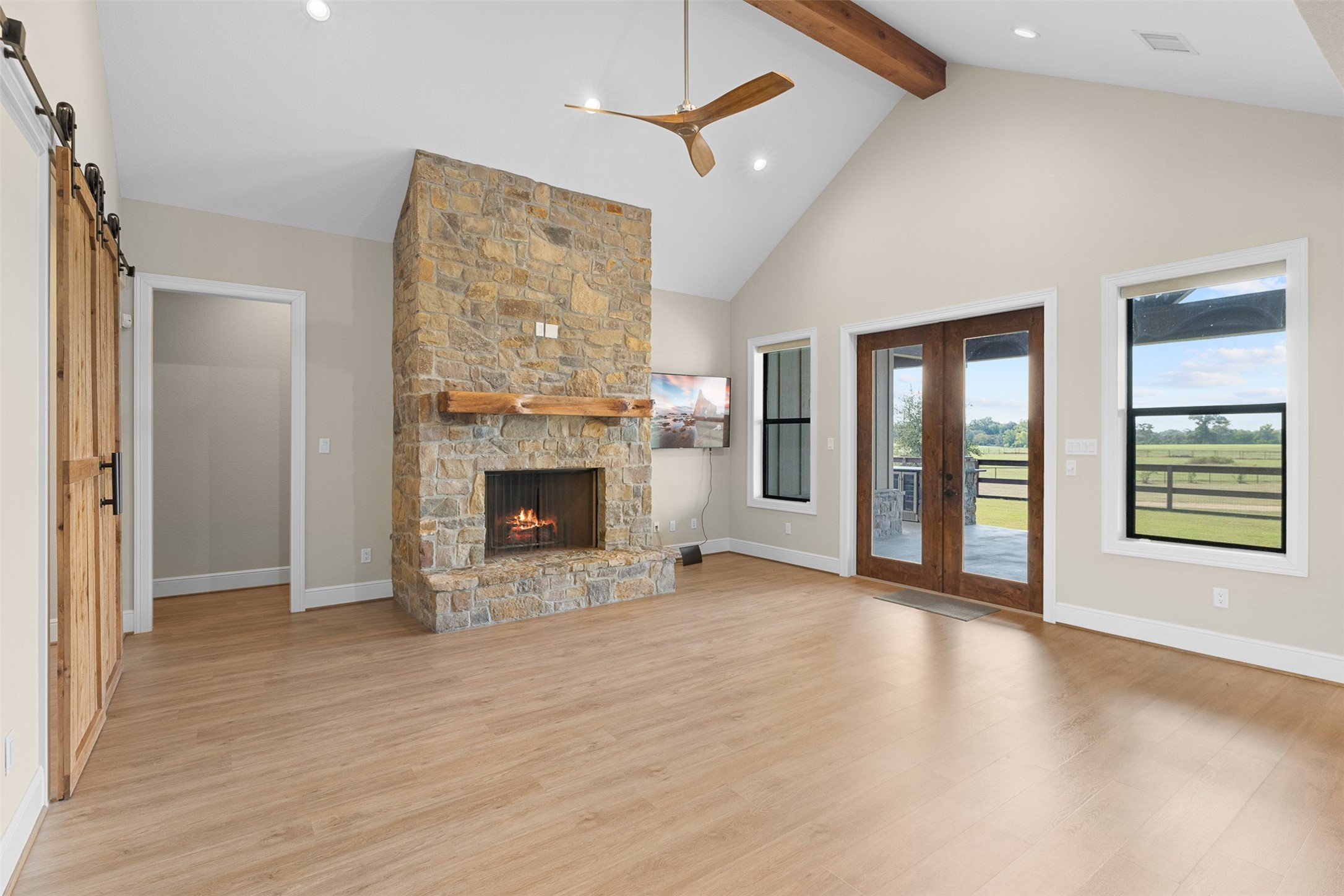 30163 High Spirit Ranch Road Hempstead, TX 77445 - Photo 9 of 46 Living room view shows the barn door entrance to the study, and hallway to the secondary bedrooms. Wooden double doors lead out to the patio and outdoor kitchen. Stone fireplace with custom wood mantle adds warmth and charm.