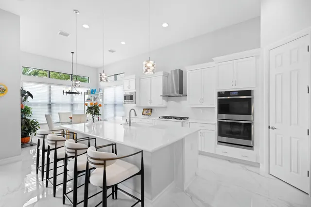 a large white kitchen with stainless steel appliances kitchen island granite countertop a white cabinets and chairs