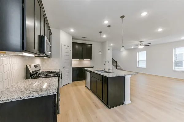 a kitchen with stainless steel appliances granite countertop a sink a stove and a wooden floor