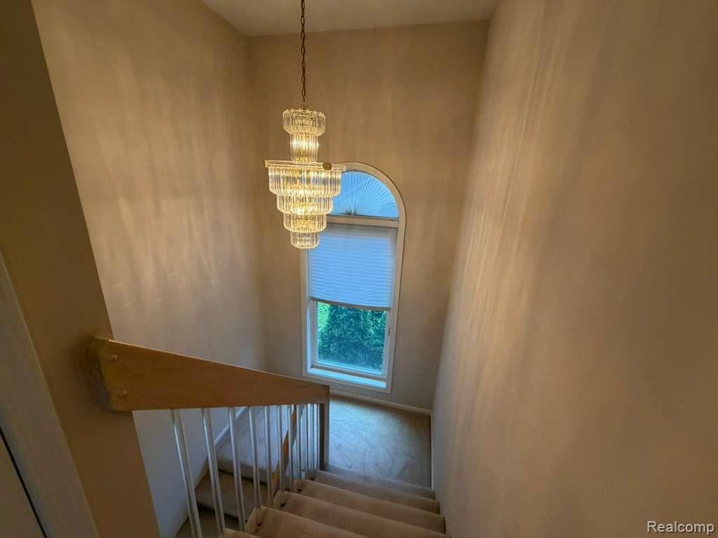 1154 Bluebird Drive Rochester, MI 48307 - Photo 30 of 34 Stairwell featuring a tiered glass chandelier, an arched window, a light wood-finish handrail, and carpeted stairs