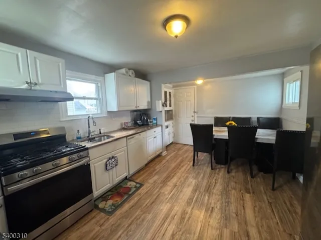 a kitchen with stainless steel appliances granite countertop a stove a sink dishwasher a microwave oven and a dining table with wooden floor