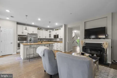 a living room with stainless steel appliances furniture a fireplace a flat screen tv and kitchen view