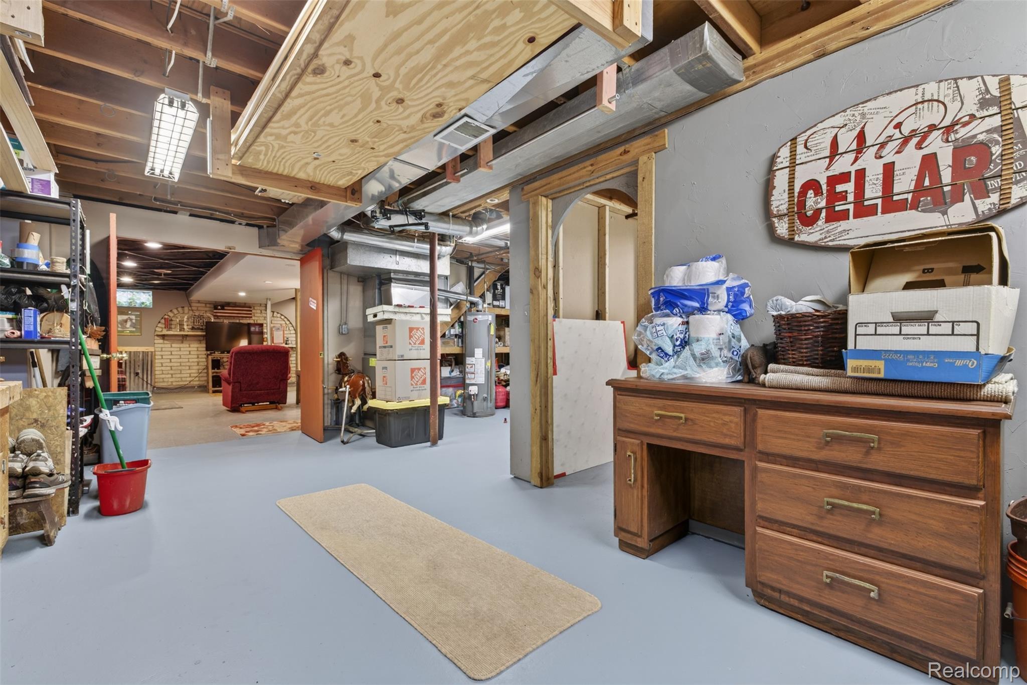 5977 Anglers Road Ortonville, MI 48462 - Photo 31 of 63 Finished basement area featuring exposed ceiling joists and ductwork, a painted concrete floor, and an arched doorway leading to a further finished space with a brick-faced wall