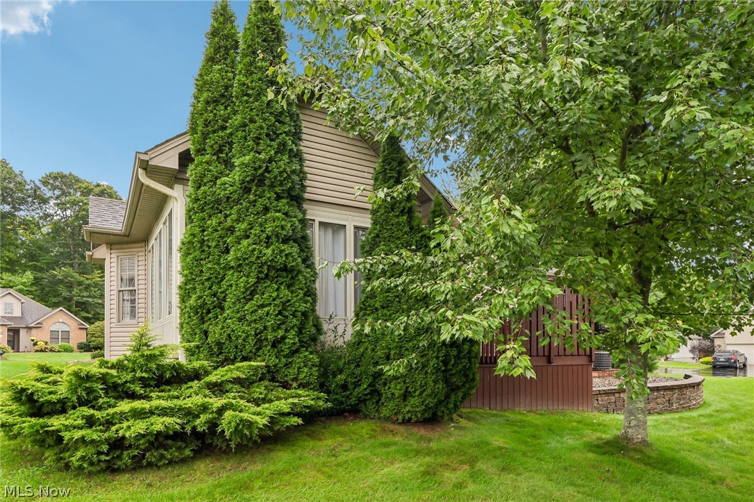 7007 Clingan Road, Unit 85 Youngstown, OH 44514 - Photo 43 of 46 Manicured lawn with mature trees and shrubbery, featuring a brown wood-paneled deck and stone retaining wall