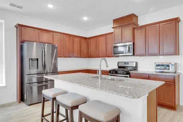 a kitchen with stainless steel appliances granite countertop a stove a sink dishwasher and a refrigerator with wooden cabinets