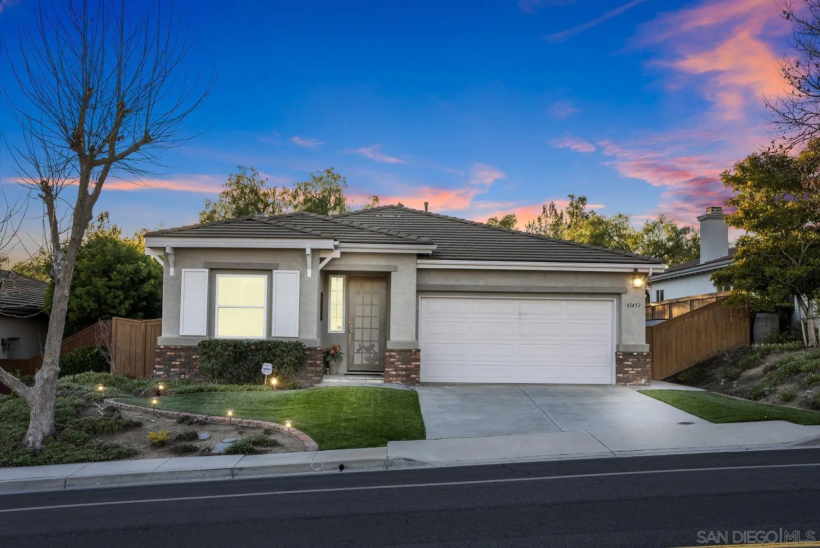 a view of a house with a yard plants and large tree