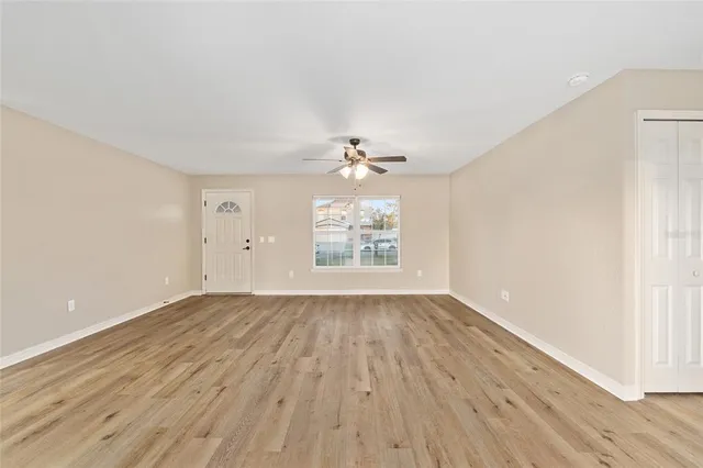 an empty room with wooden floor chandelier fan and windows