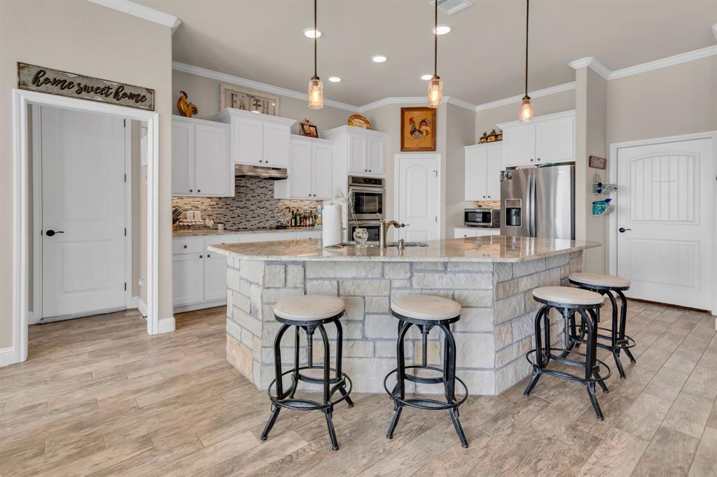 7728 County Road 1205 Rio Vista, TX 76093 - Photo 14 of 31 Kitchen featuring decorative backsplash, white cabinetry, pendant lighting, a breakfast bar, and ornamental molding