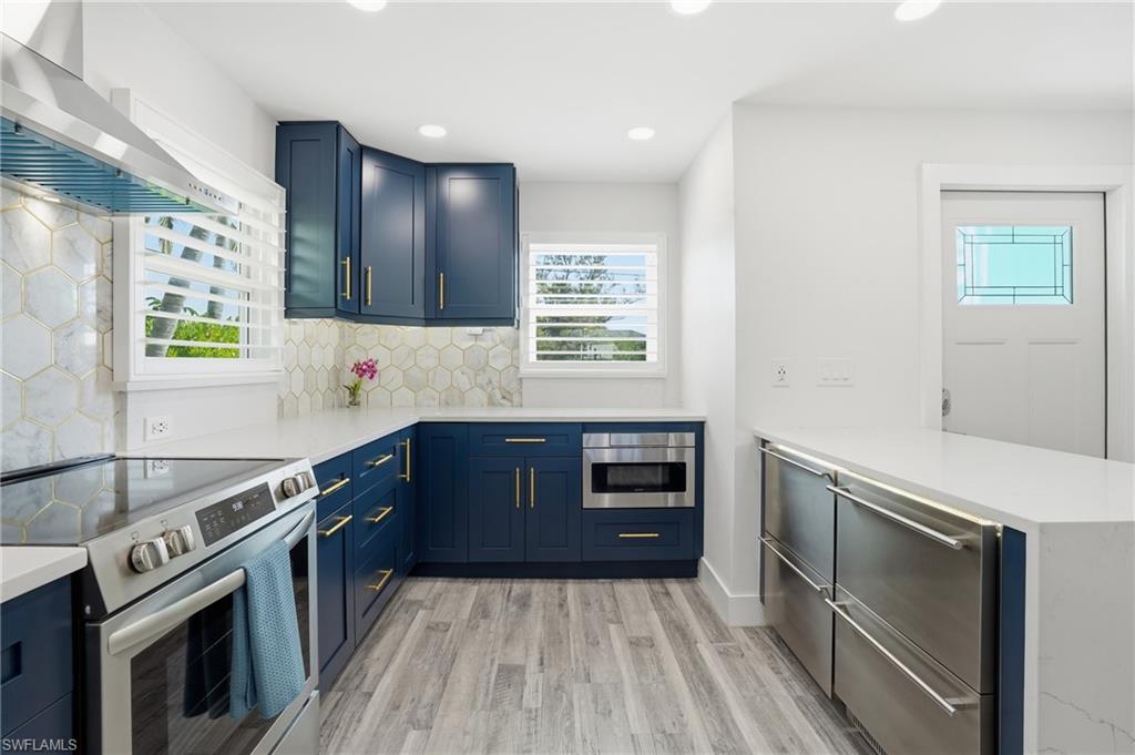 270 Dundee Road Fort Myers Beach, FL 33931 - Photo 16 of 48 Kitchen featuring stainless steel appliances, a peninsula, wall chimney exhaust hood, blue cabinets, and recessed lighting - Virtually Edited Image