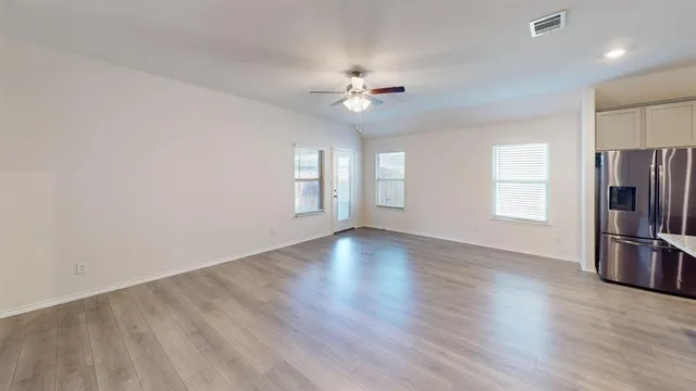 an empty room with wooden floor a ceiling fan and windows