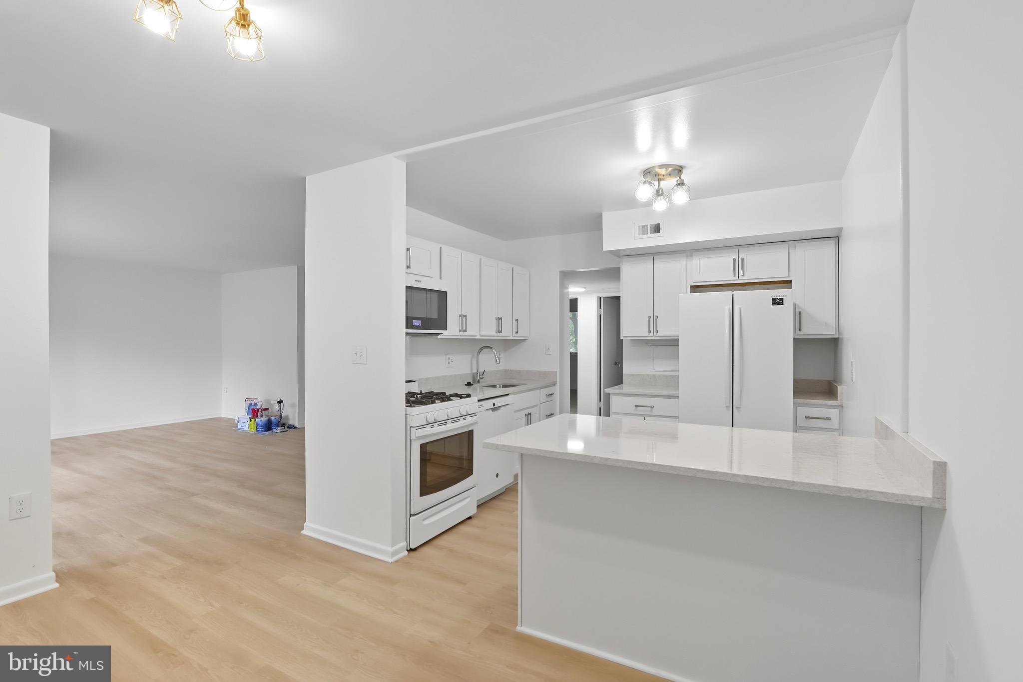 a large white kitchen with a stove a sink dishwasher and a refrigerator with wooden floor