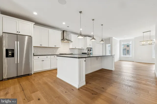 a kitchen with stainless steel appliances granite countertop a refrigerator a sink dishwasher a stove and white cabinets with wooden floor