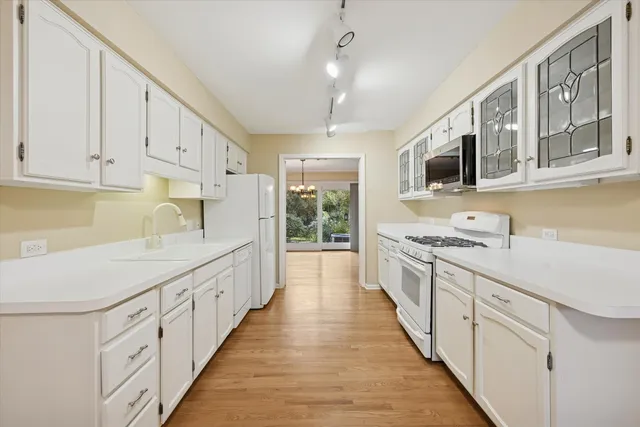 a large white kitchen with granite countertop a stove top oven a sink dishwasher and white cabinets with wooden floor
