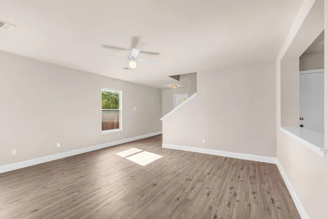 an empty room with wooden floor ceiling fan and windows