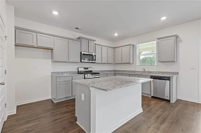 a kitchen with stainless steel appliances granite countertop a sink a stove a refrigerator and white cabinets