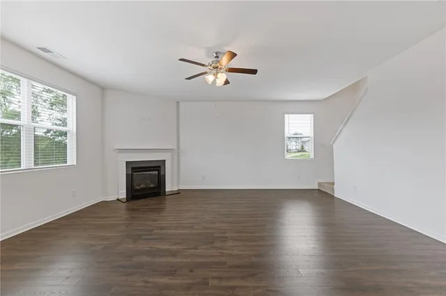 an empty room with wooden floor chandelier fan and windows