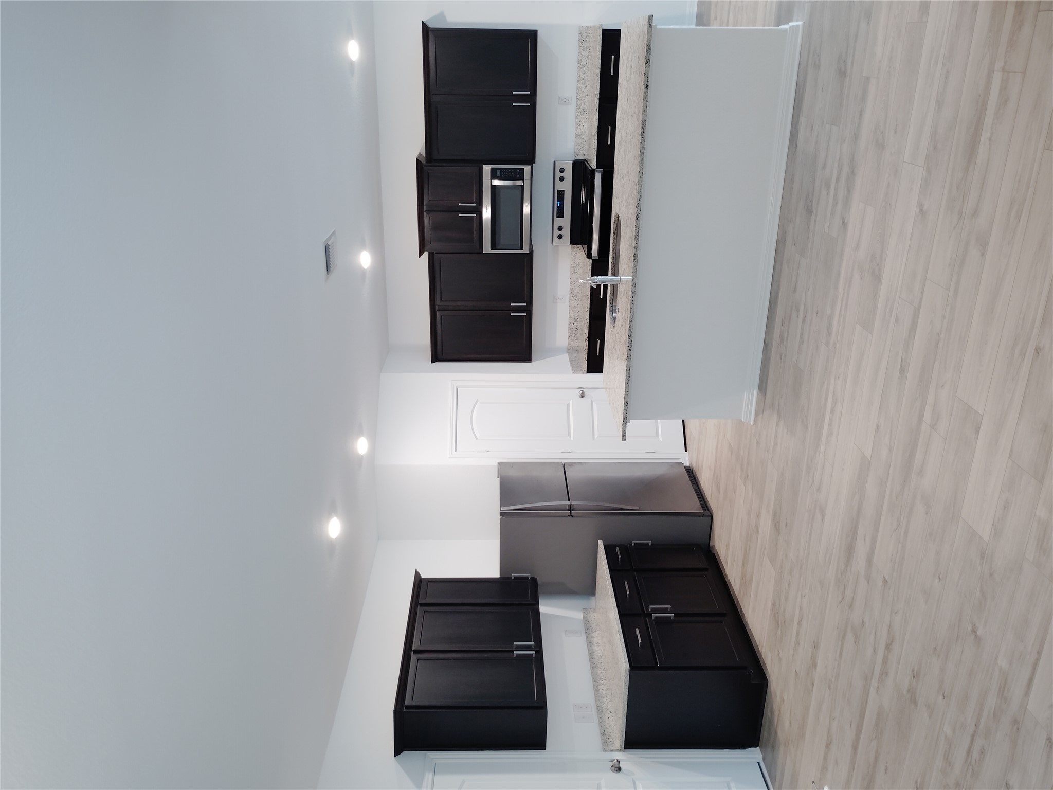 14024 Prairie Schooner Pass Elgin, TX 78621 - Photo 6 of 20 Kitchen featuring dark cabinetry, stainless steel appliances, speckled countertops, a central island with a sink, and light wood-finish flooring