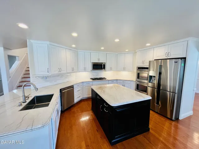 a large kitchen with stainless steel appliances granite countertop a stove a sink a refrigerator and white cabinets