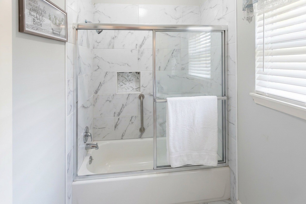 206 Riverside Street Highlands, TX 77562 - Photo 8 of 12 Beautifully updated full bath featuring a tub/shower combo with floor to ceiling marble look tile surround, sliding glass doors, and a built in niche . Clean, modern, and move in ready.