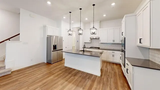 a kitchen with stainless steel appliances kitchen island granite countertop a refrigerator a sink and white cabinets