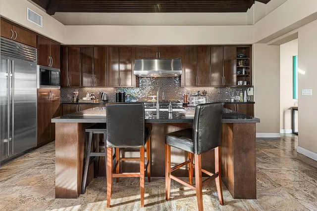 a kitchen with stainless steel appliances granite countertop a dining table chairs refrigerator and sink