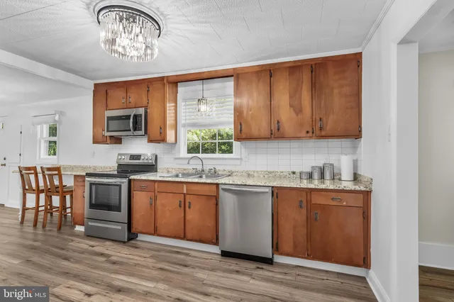 a kitchen with stainless steel appliances granite countertop a stove top oven a sink dishwasher a dining table and chairs with wooden floor