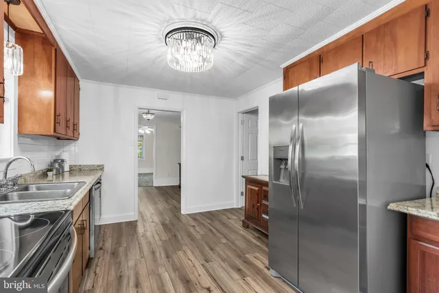 a kitchen with stainless steel appliances granite countertop a refrigerator a stove and a sink with wooden floor