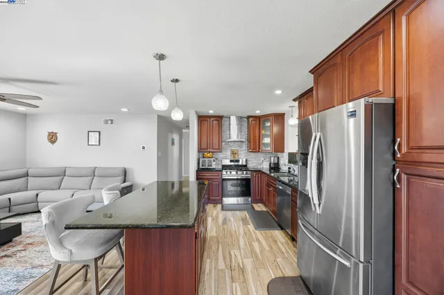 a kitchen with stainless steel appliances granite countertop a refrigerator a oven a sink a dining table and chairs with wooden floor