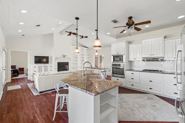 a large kitchen with kitchen island a stove a sink a oven and a dining table with white cabinets