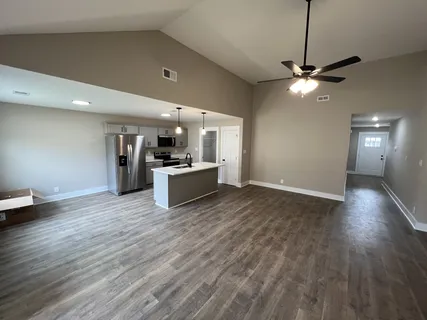 a view of an empty room and kitchen with wooden floor