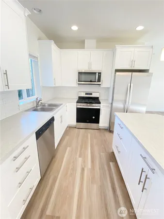 a large kitchen with stainless steel appliances granite countertop a refrigerator a sink dishwasher a stove and white countertops with wooden floor