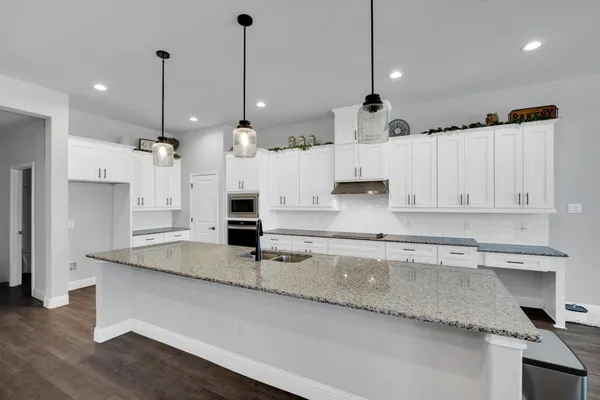 a large kitchen with granite countertop a white sink and white cabinets