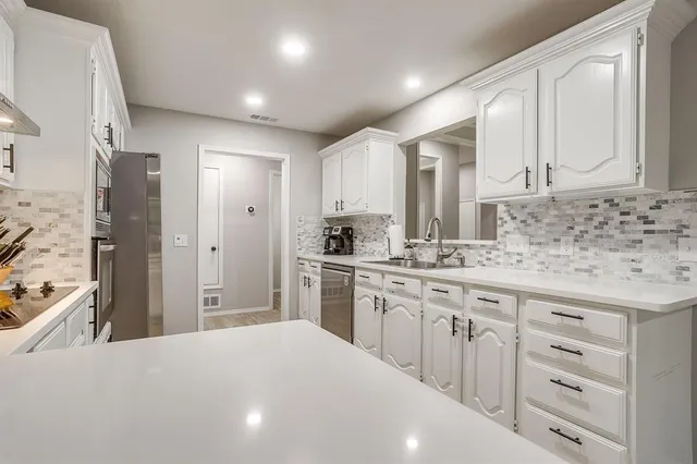 a kitchen with granite countertop a sink stove refrigerator and white cabinets with wooden floor