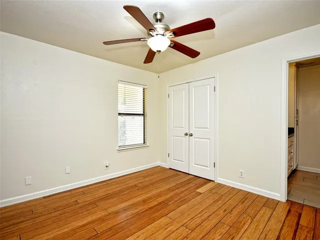 a view of an empty room with wooden floor and a ceiling fan