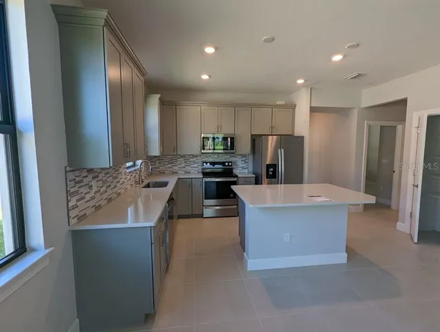 a large kitchen with stainless steel appliances kitchen island granite countertop a refrigerator a stove and a sink with large window