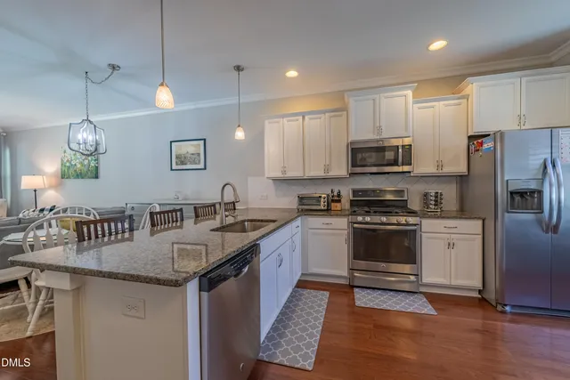 a kitchen with stainless steel appliances granite countertop a sink a stove a refrigerator cabinets and a dining table